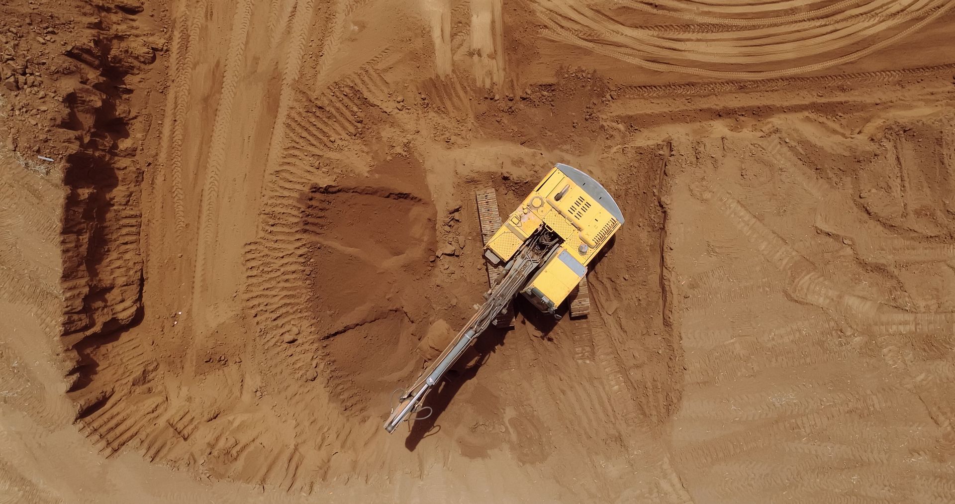 Yellow excavator digging in a large dirt pit, viewed from above.
