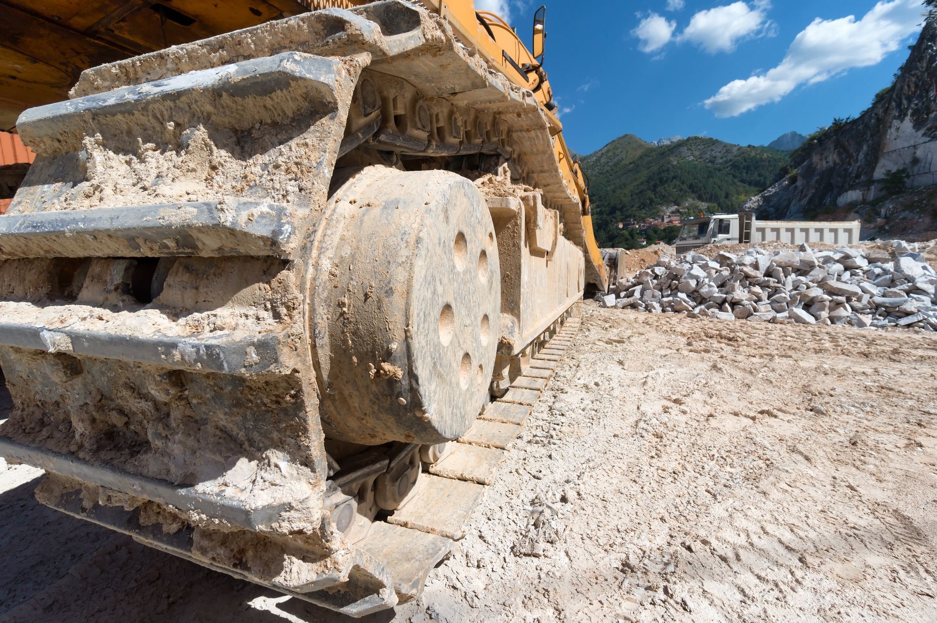 Tracked excavator on a rocky construction site with mountains and blue sky in the background