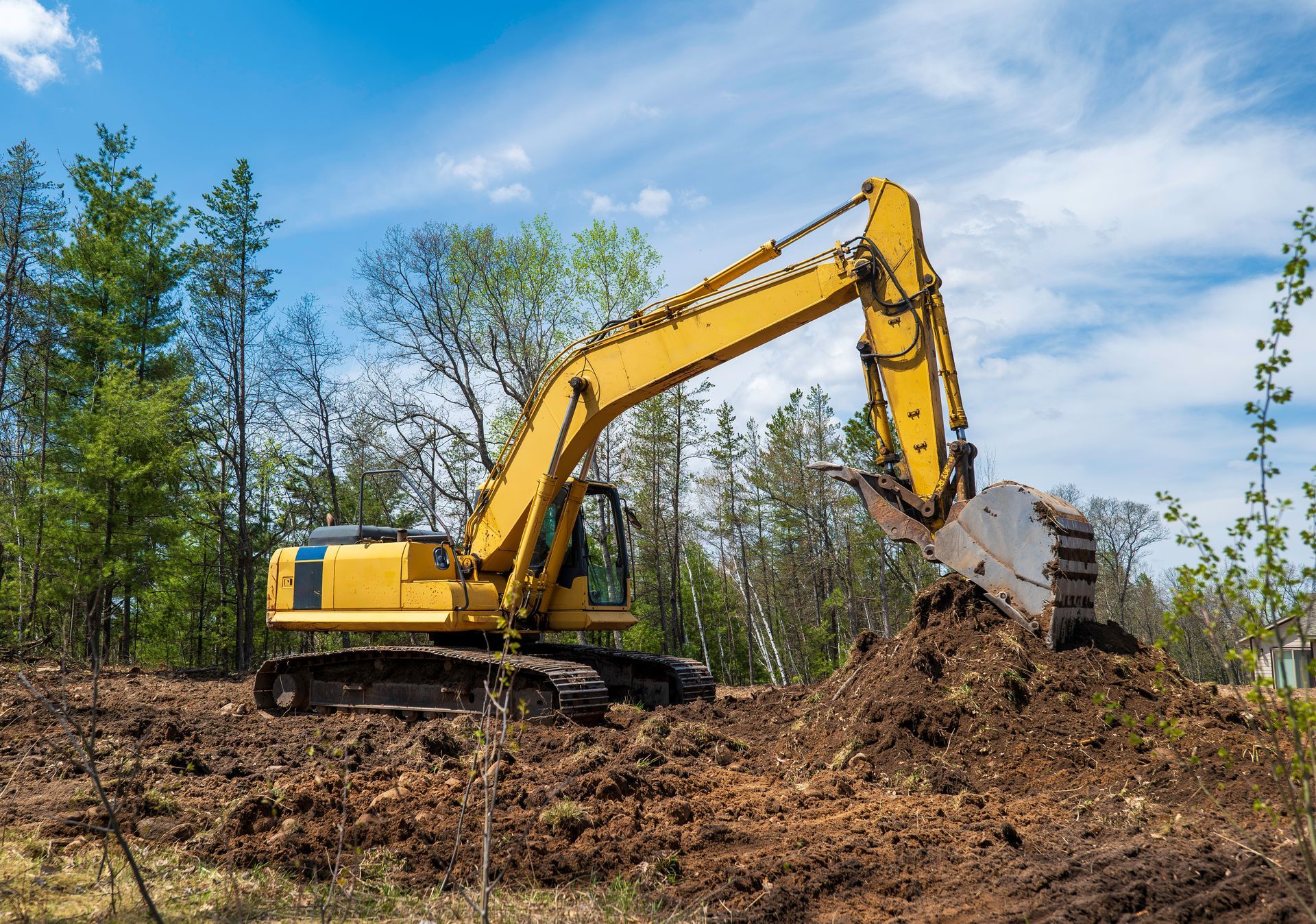 Yellow excavator digging soil in a wooded construction site