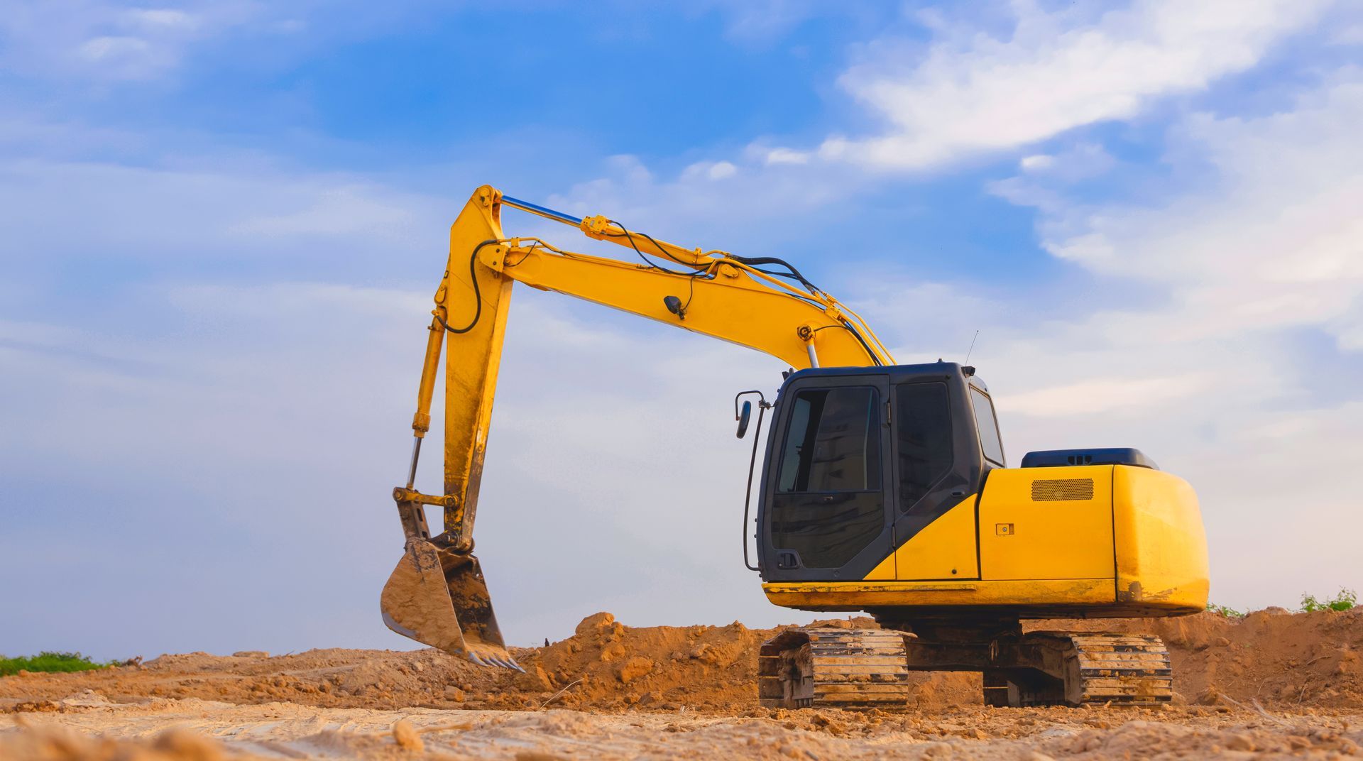 Yellow excavator digging on a dirt construction site under a blue sky.