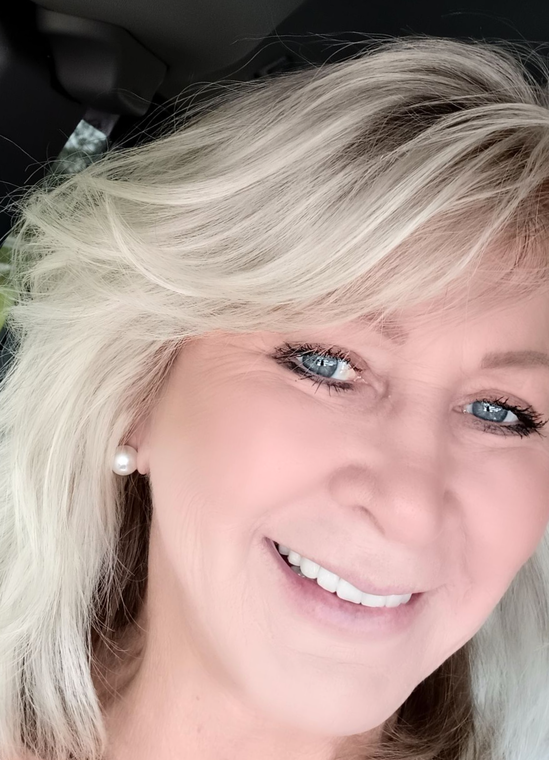 A smiling person with blonde hair and pearl earrings, captured in a close-up portrait.