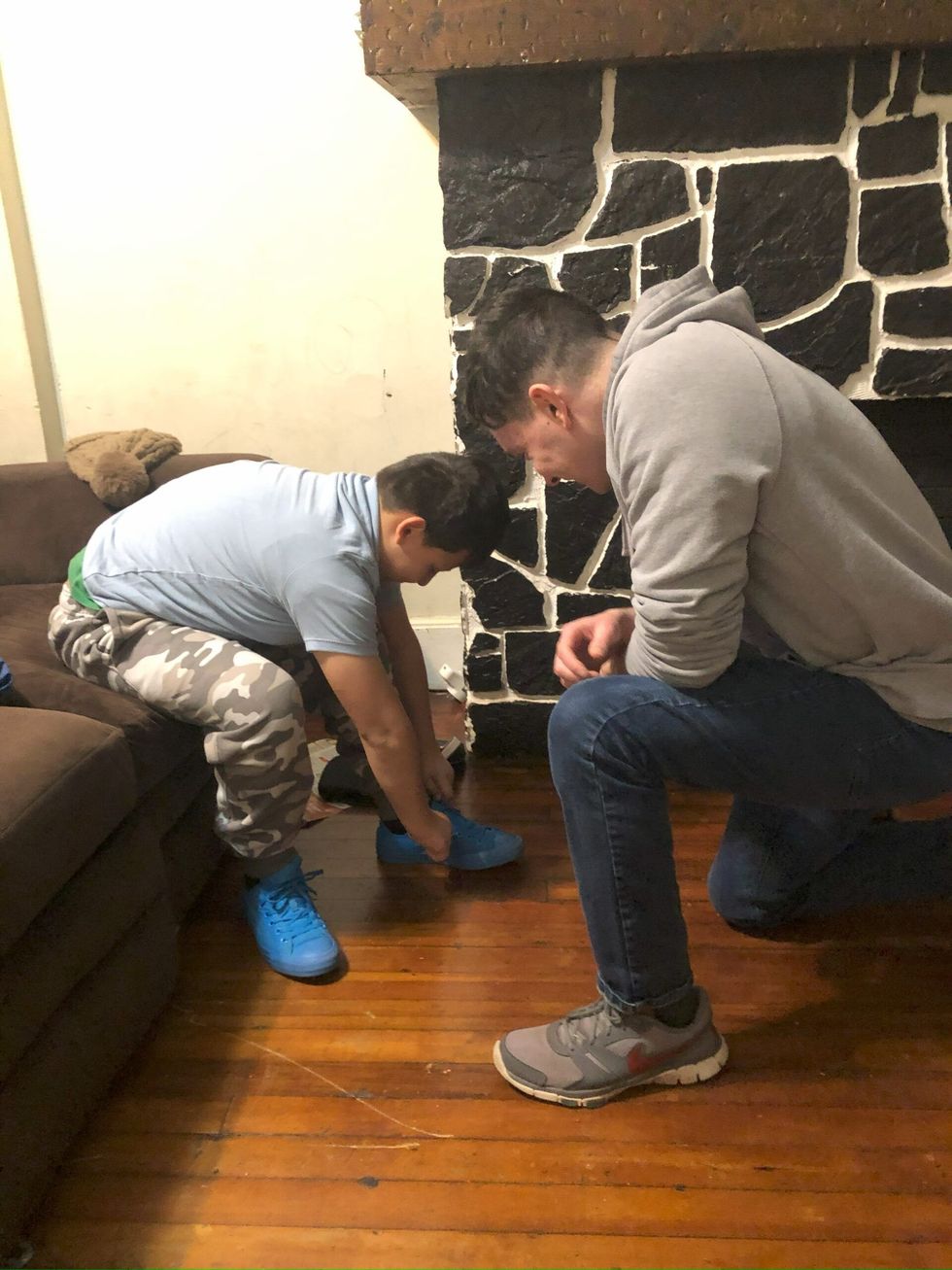 A man is kneeling down next to a boy who is tying his shoes.