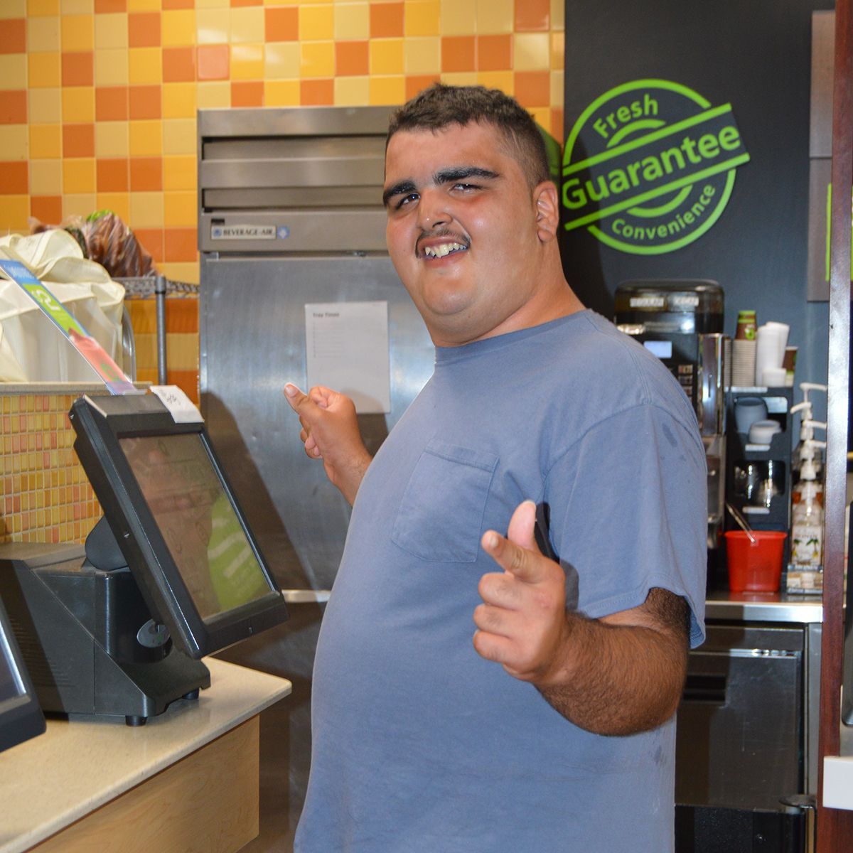 A man giving a thumbs up in front of a sign that says fresh guarantee