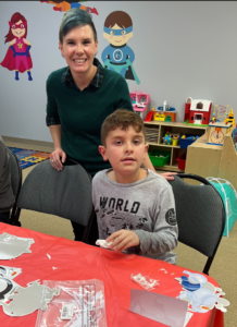 A boy wearing a world shirt sits at a table with a woman