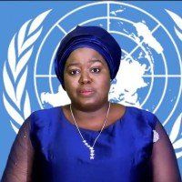 Une femme en robe bleue se tient devant un drapeau des Nations Unies.
