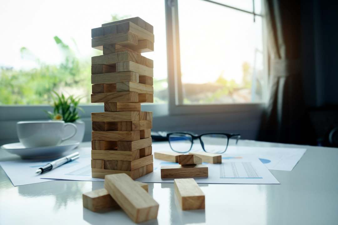 Une tour de Jenga dont il a été retiré des blocs, posée sur un bureau avec une plante, une tasse de café, des verres.