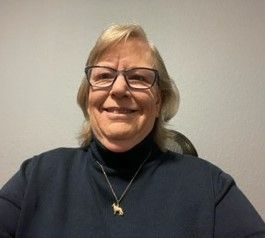 A woman wearing glasses and a necklace is smiling for the camera.