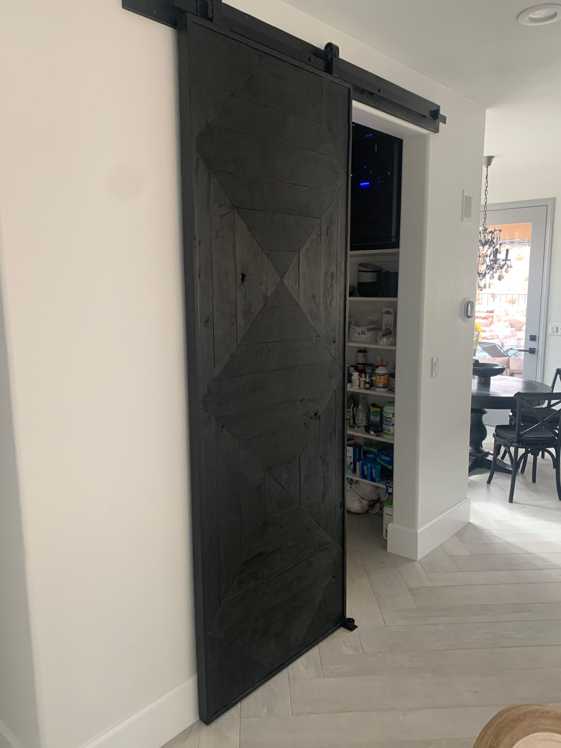 Black sliding barn door partially open in a bright hallway, revealing a cluttered closet and adjacent room.