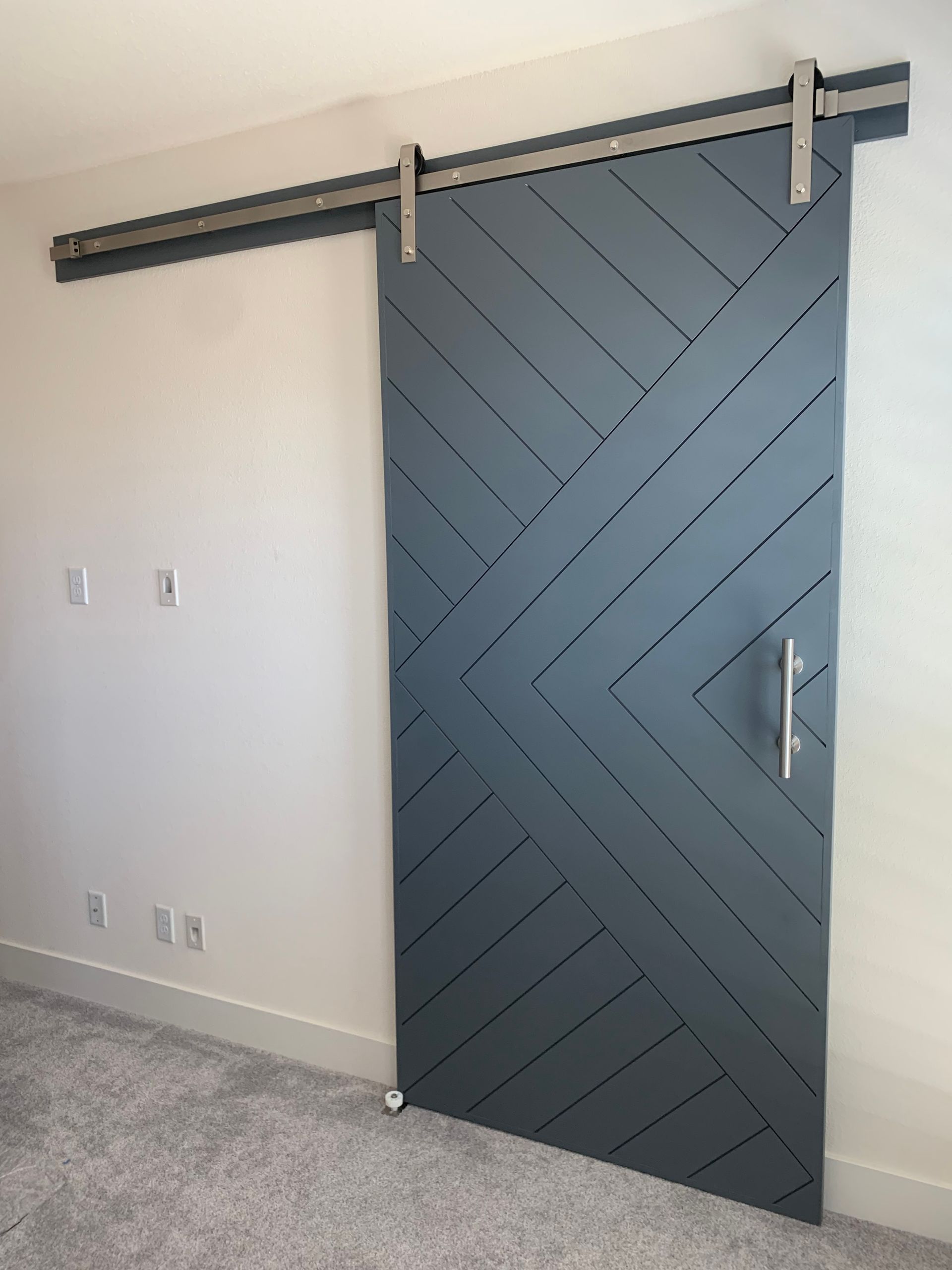 Gray sliding barn door with diagonal slats and metal hardware in a white room