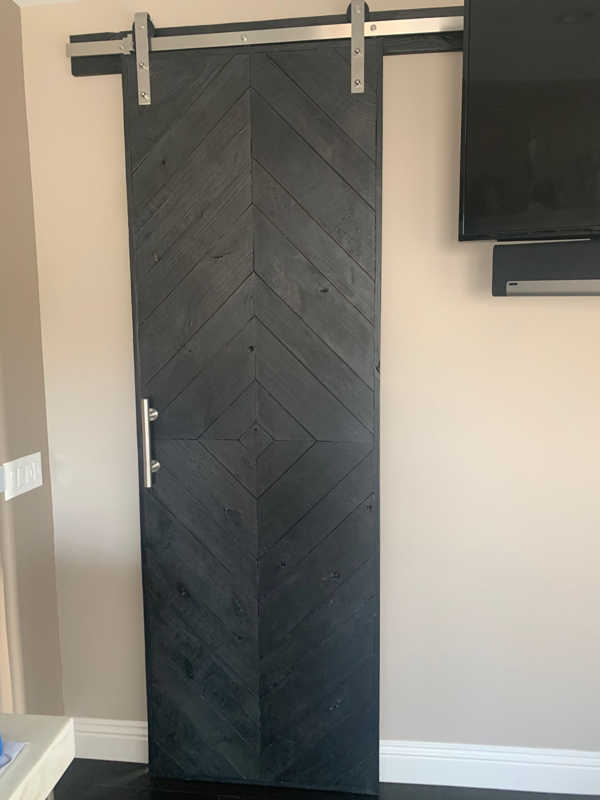 Black barn-style sliding door on a beige wall with a TV mounted to the right.