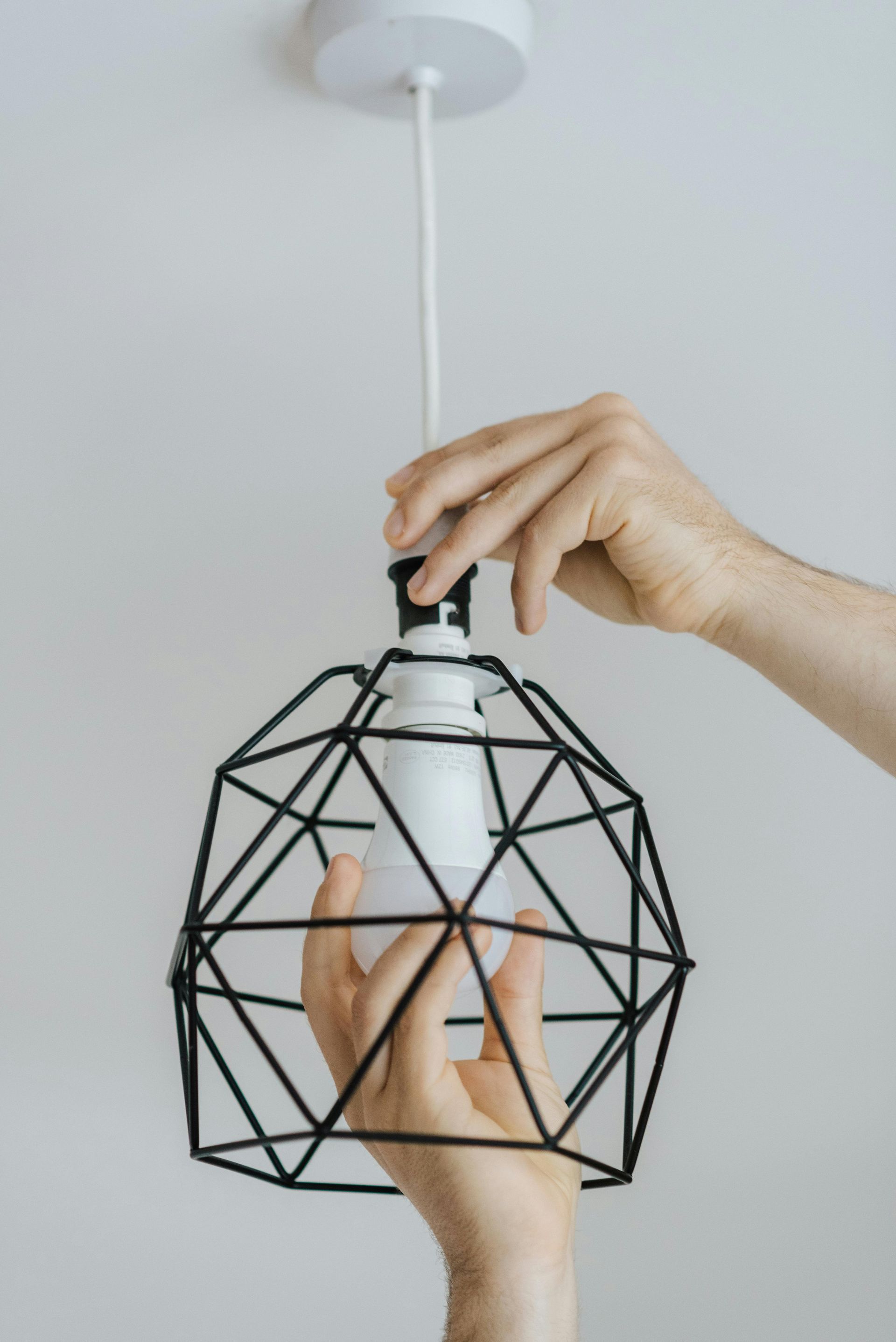 Hand placing a white bulb into a black geometric pendant lamp fixture