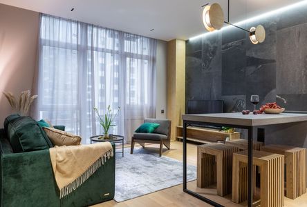 Modern living room with green sofa, large window, glass dining table, and wooden stools