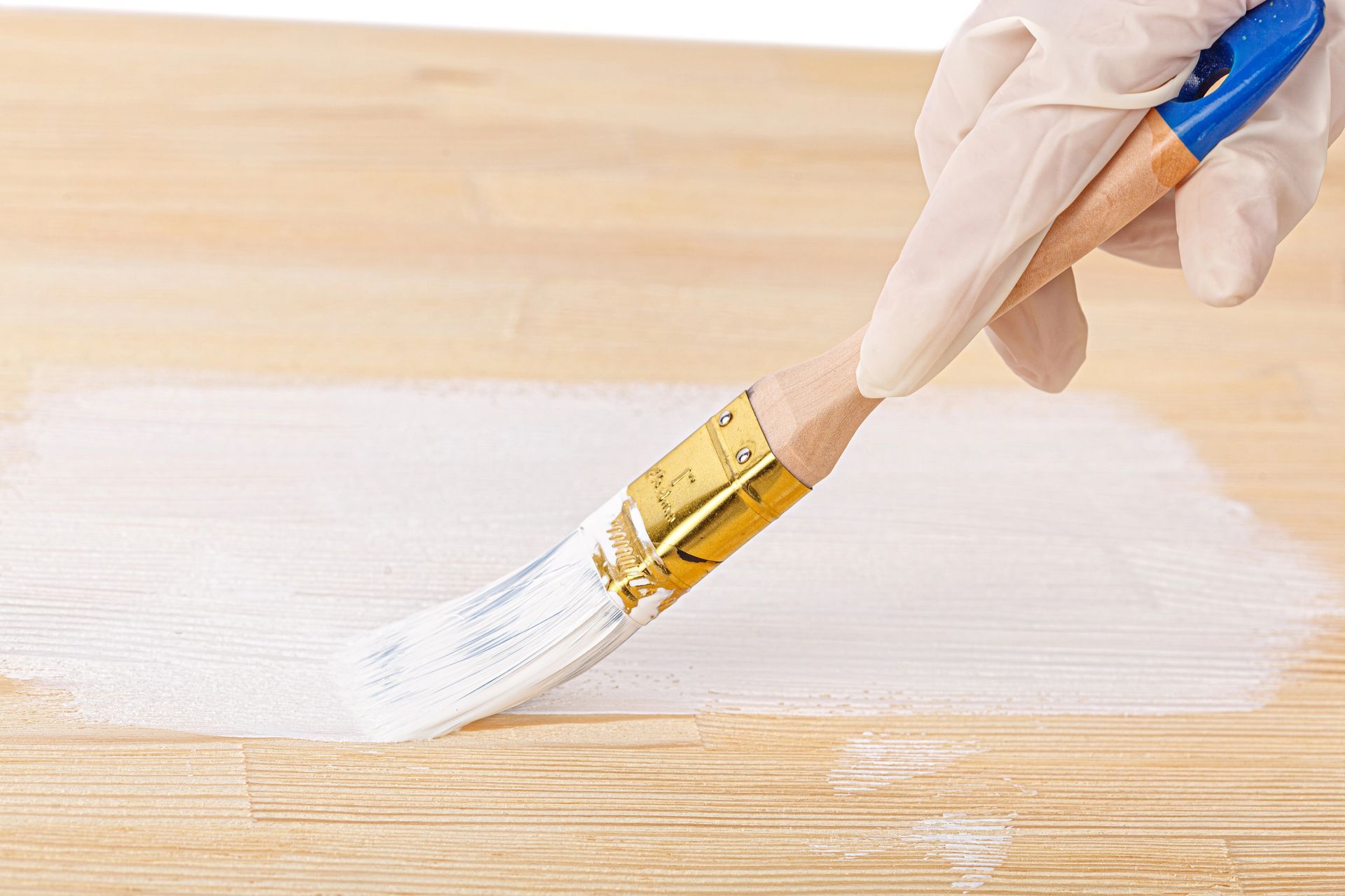 Mano guantata che dipinge una superficie di legno con un pennello bianco