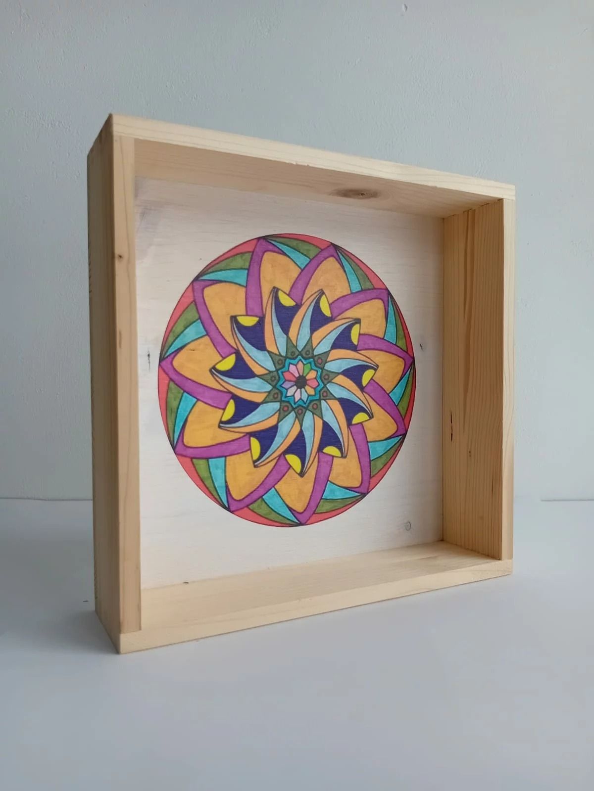 Cornice in legno con un mandala circolare astratto e colorato su sfondo bianco.