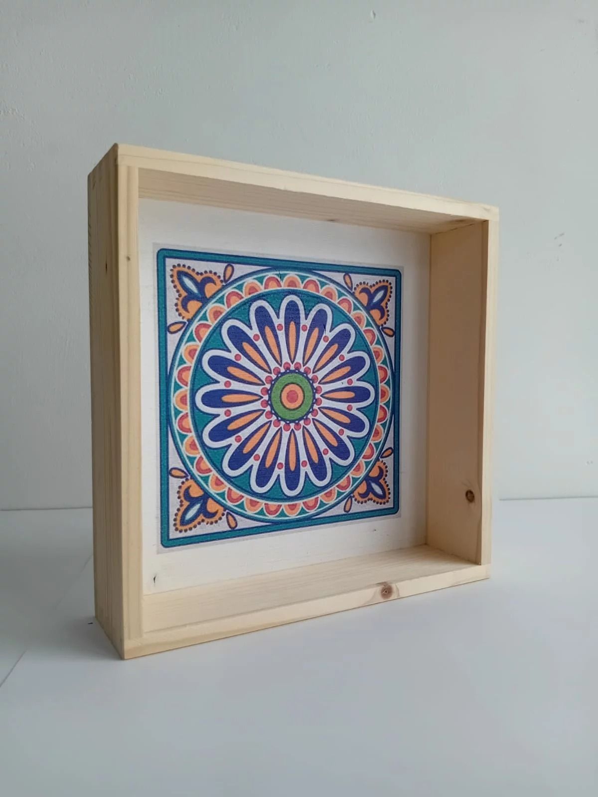 Cornice a scatola in legno con un disegno di mandala blu, rosa e arancione all'interno.