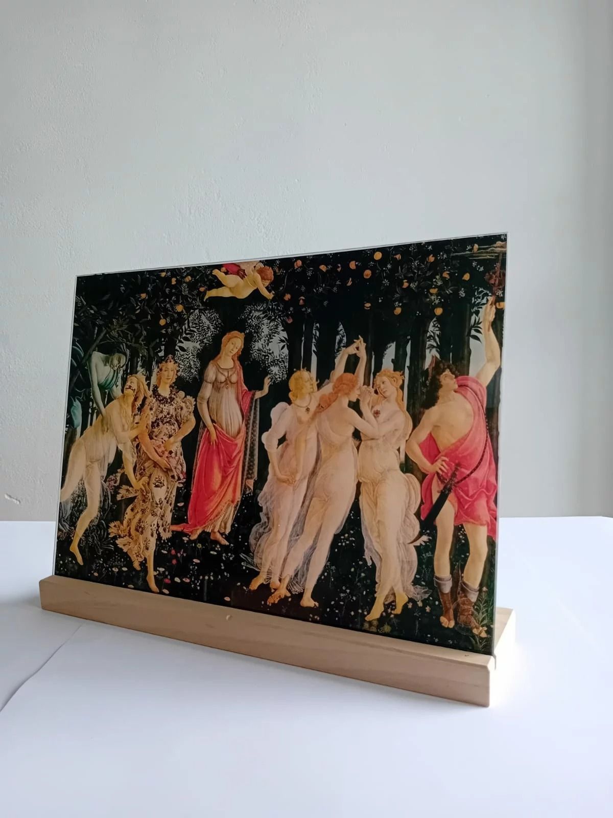 Stampa decorativa raffigurante figure danzanti su un supporto di legno, su uno sfondo chiaro.