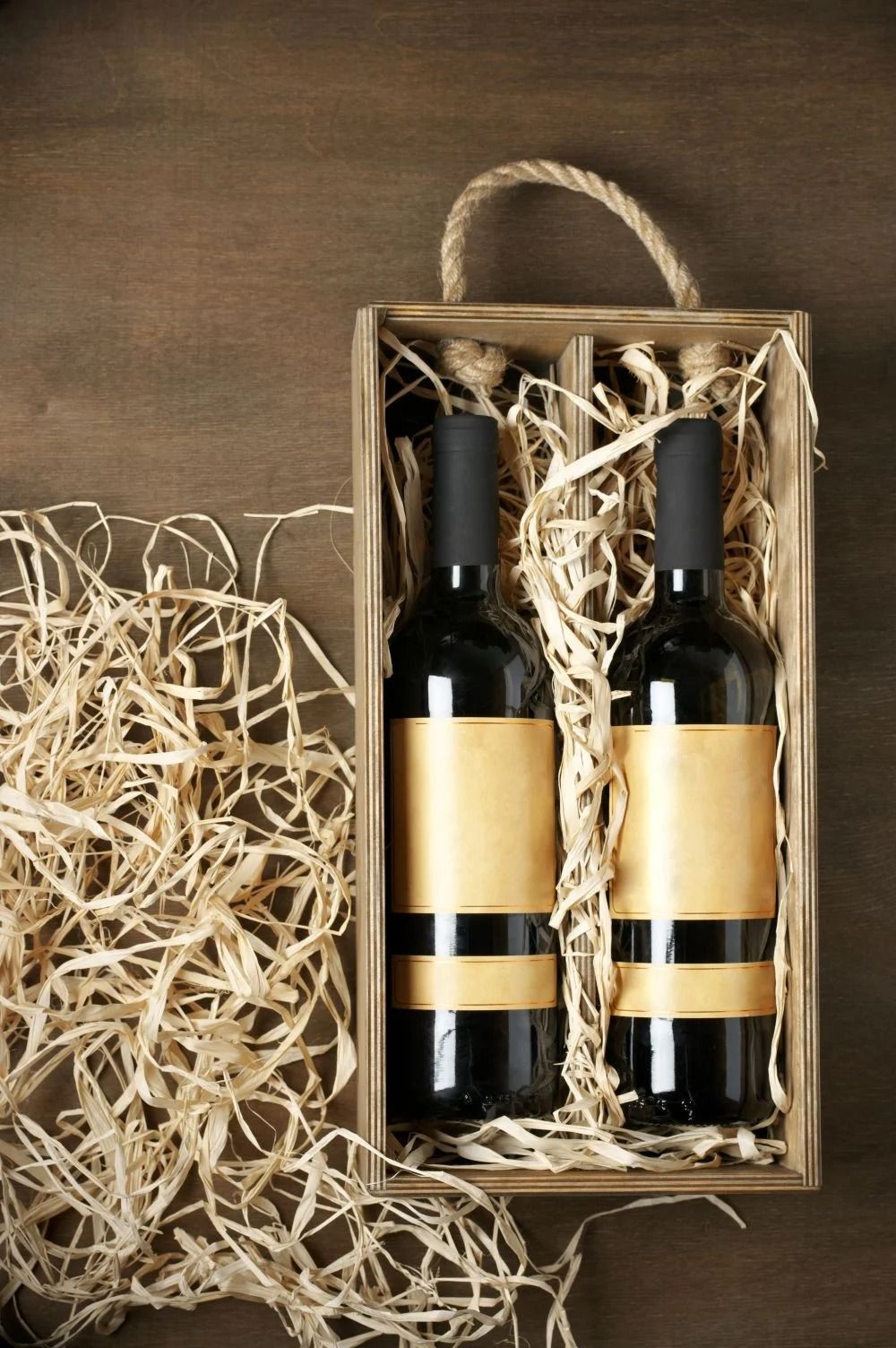 Due bottiglie di vino in un cesto regalo di vimini con imbottitura di paglia su sfondo marrone.