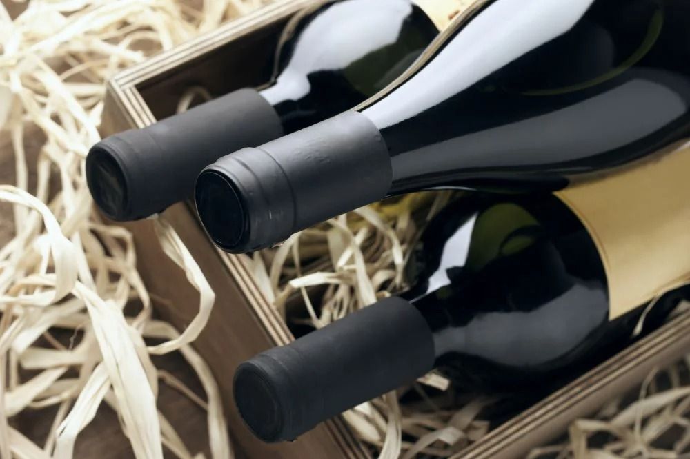 Tre bottiglie di vino su un imballaggio di paglia, viste da vicino con etichette nere e oro.