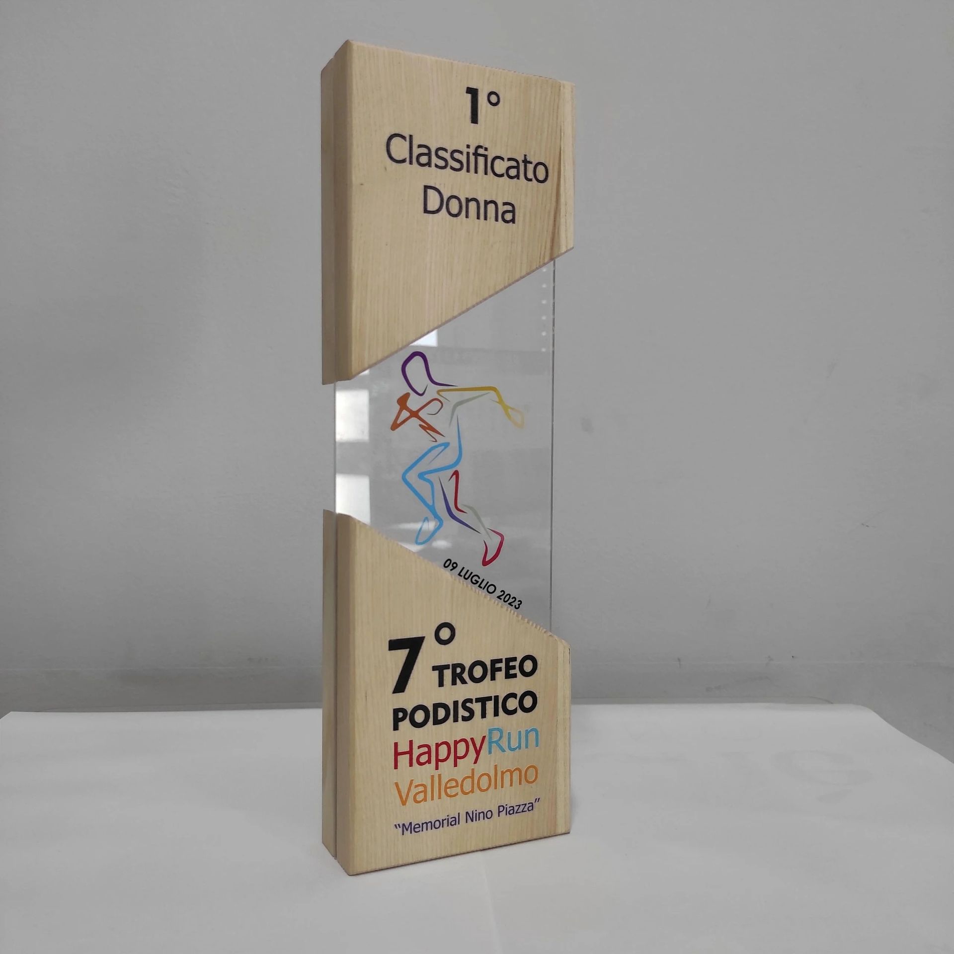 Trofeo in legno con pannello centrale trasparente e decorazioni a tratto colorate, con scritte in italiano, su sfondo bianco.