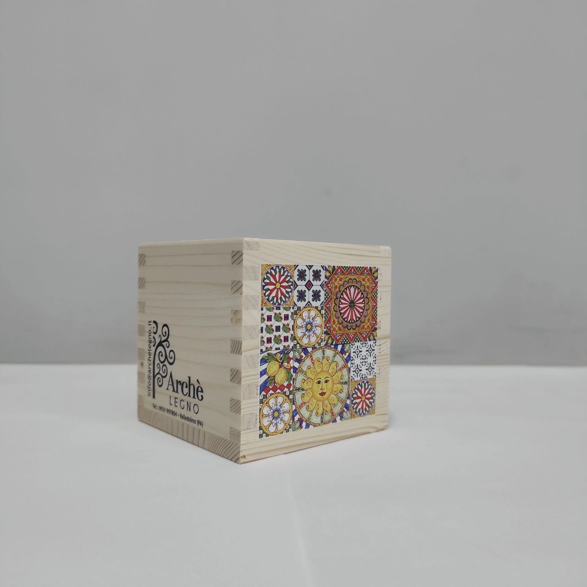 Piccolo cubo color crema con un disegno colorato in stile mosaico su un lato, poggiato su una superficie grigia.