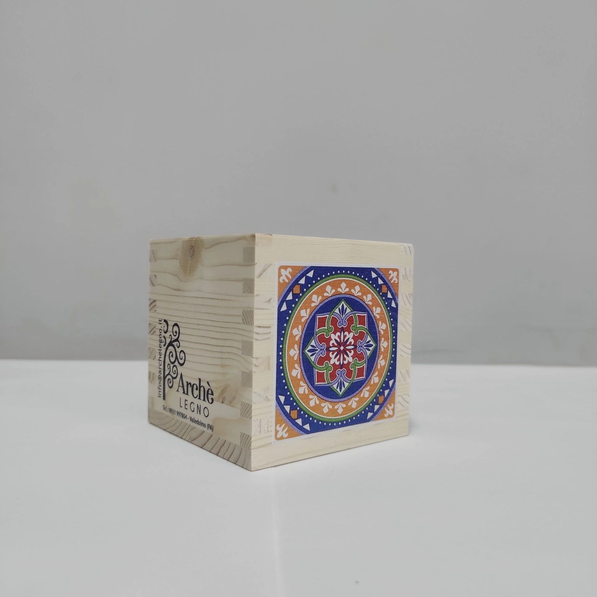 Cubo decorativo in legno con un'illustrazione colorata in stile mandala su una superficie bianca liscia.