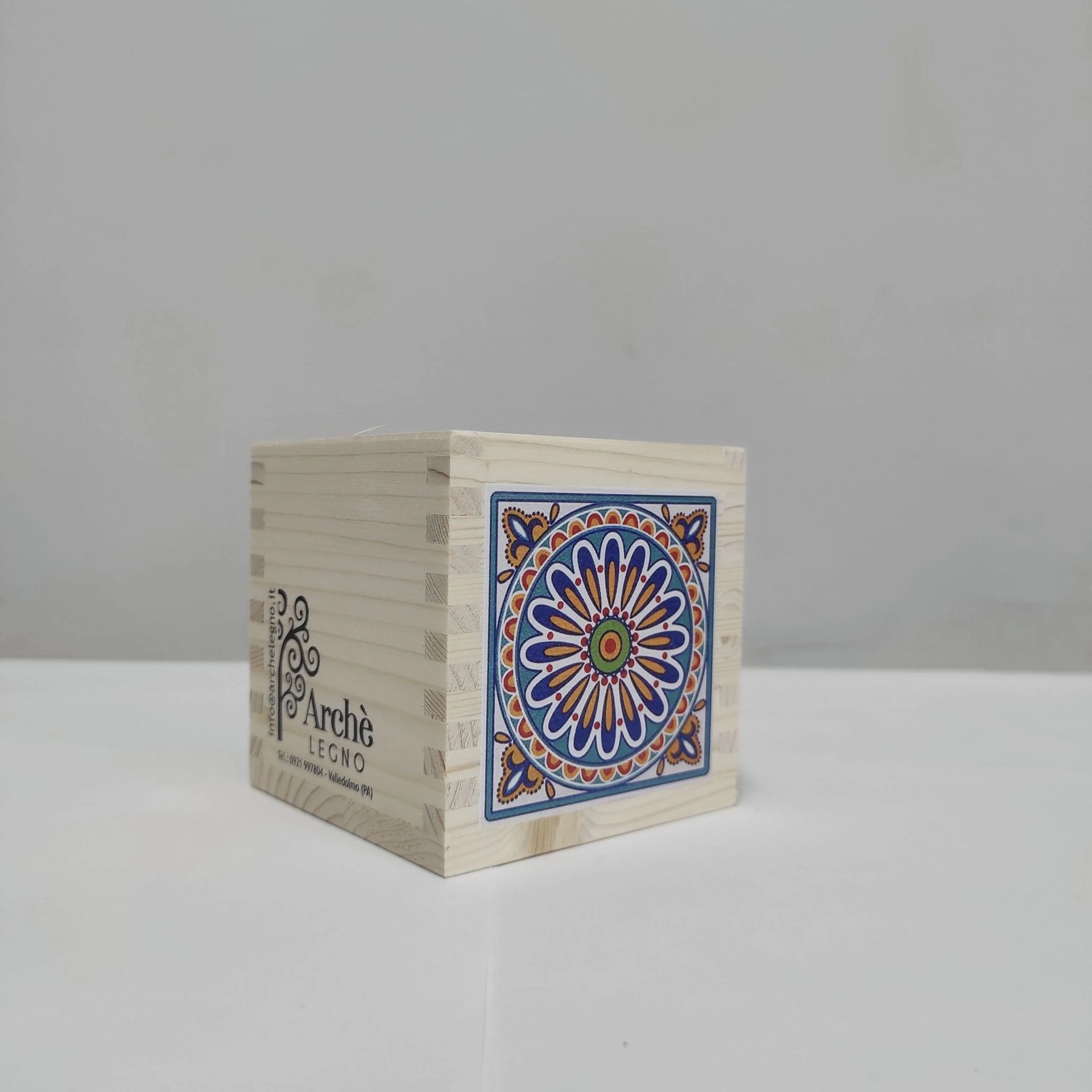 Piccola scatola cubica beige con un colorato disegno floreale a mandala blu, arancione e rosso su un lato