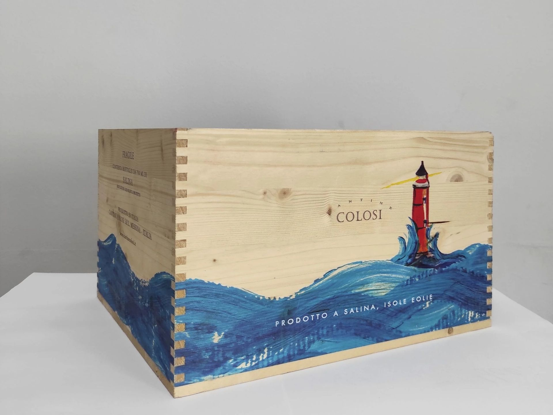 Scatola di legno con un'onda blu dipinta e un faro rosso su sfondo chiaro.