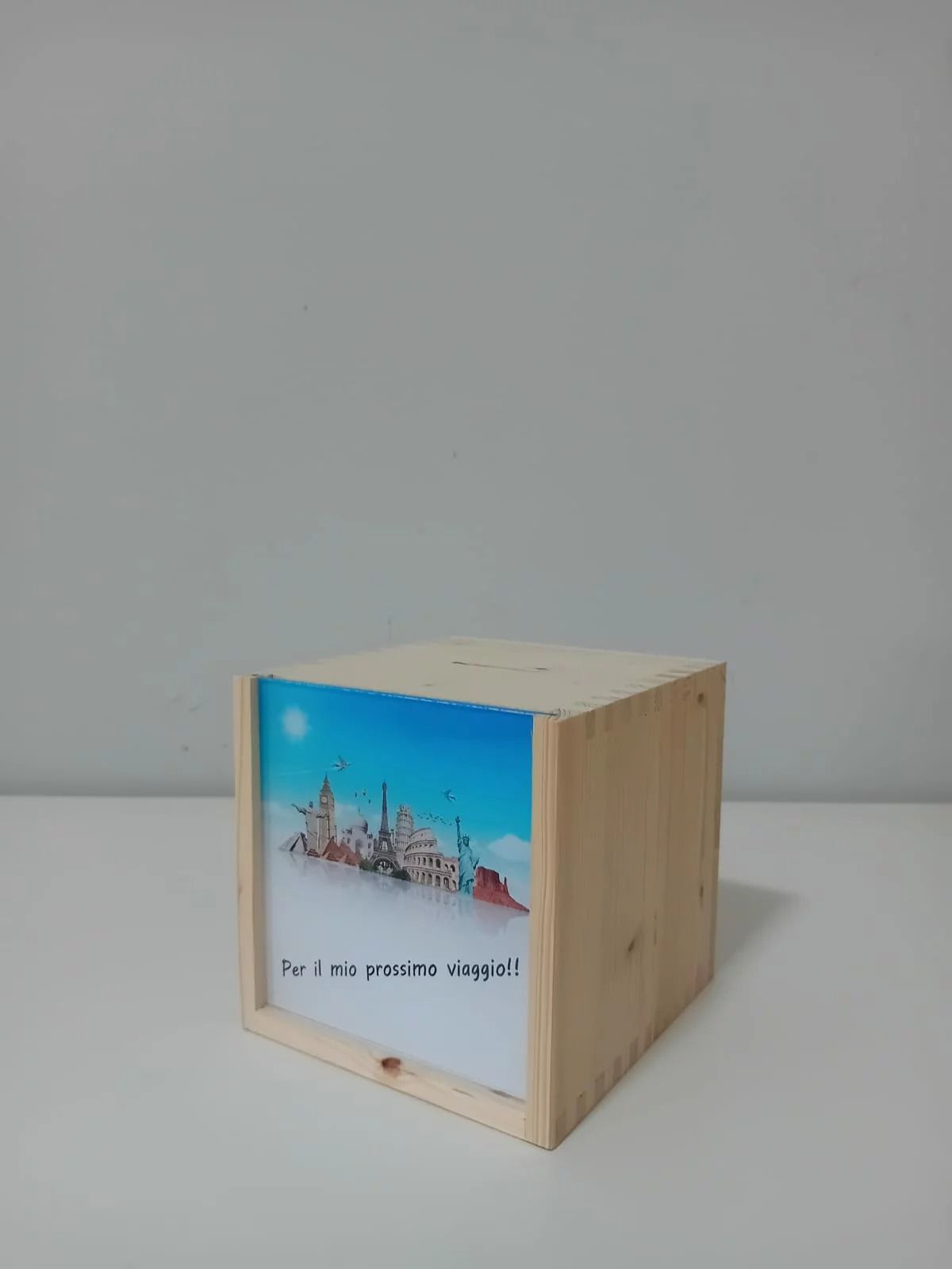 Cubo di legno con una stampa colorata di un paesaggio urbano sul davanti, appoggiato su una superficie grigio chiaro.