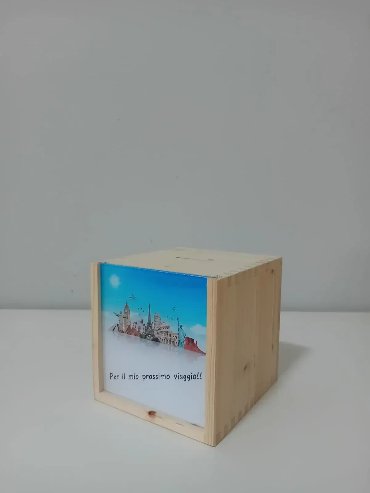 Cassa cubica in legno con una grafica raffigurante uno scenario urbano blu sulla parte anteriore, appoggiata su una superficie bianca.