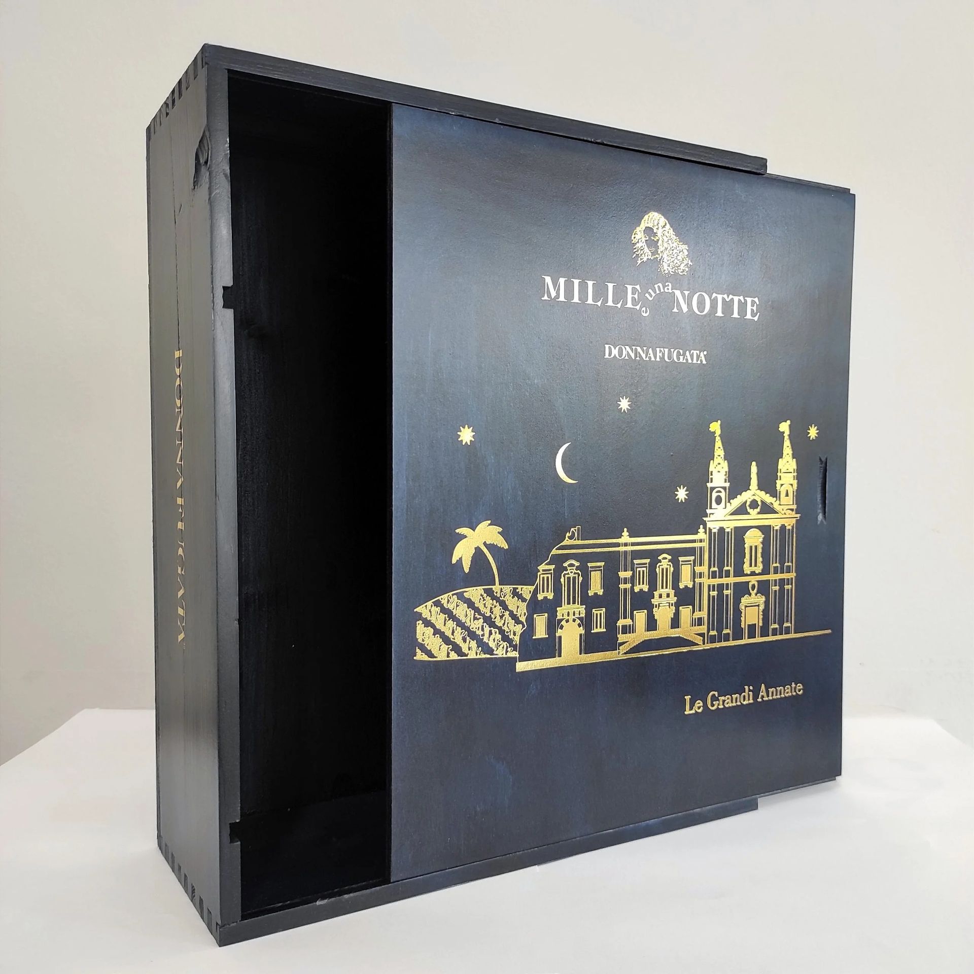 Elegante cofanetto regalo nero con decorazione dorata raffigurante luna ed edifici, parzialmente aperto su sfondo chiaro.