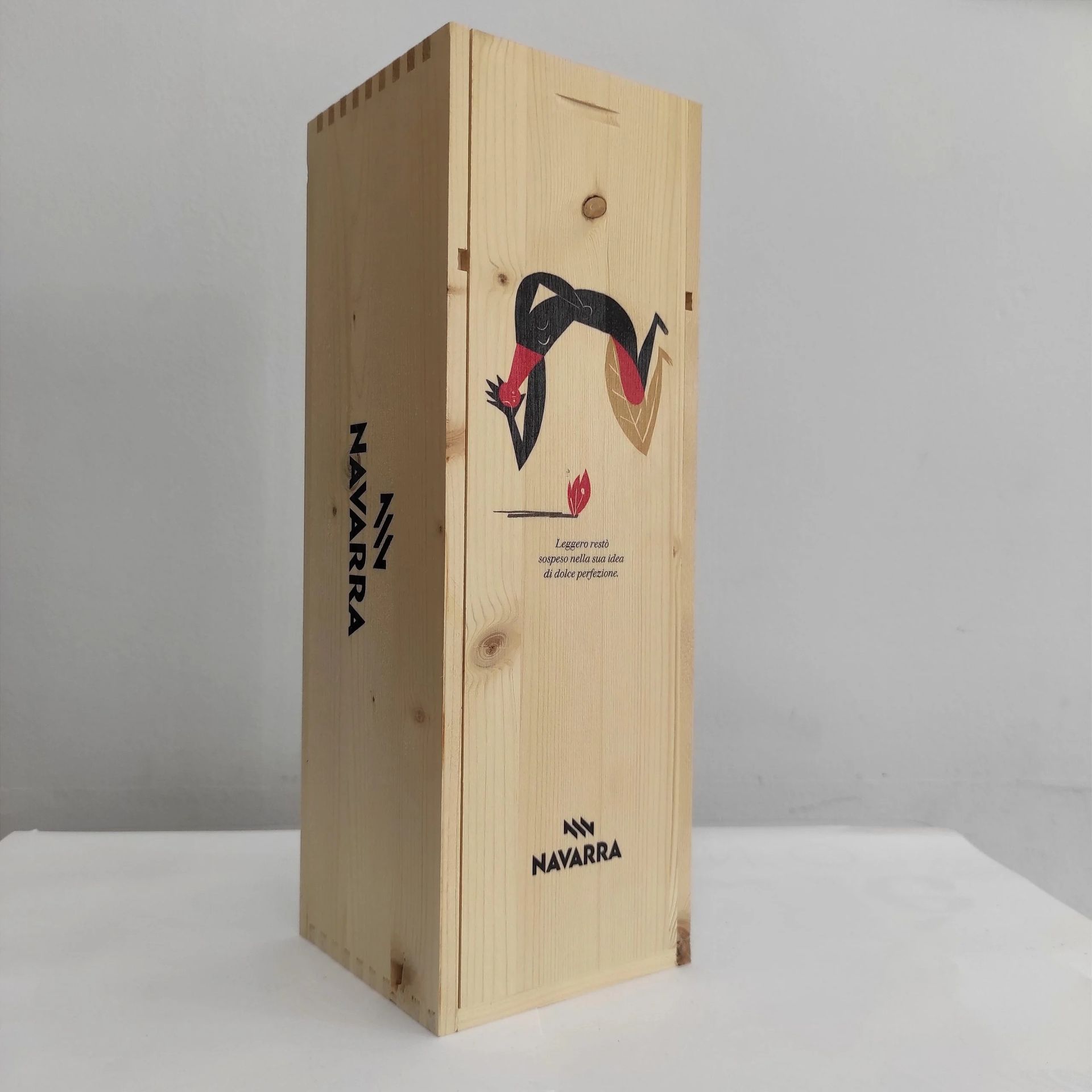 Scatola rettangolare alta in legno con logo nero e rosso, appoggiata su una superficie bianca su sfondo grigio.