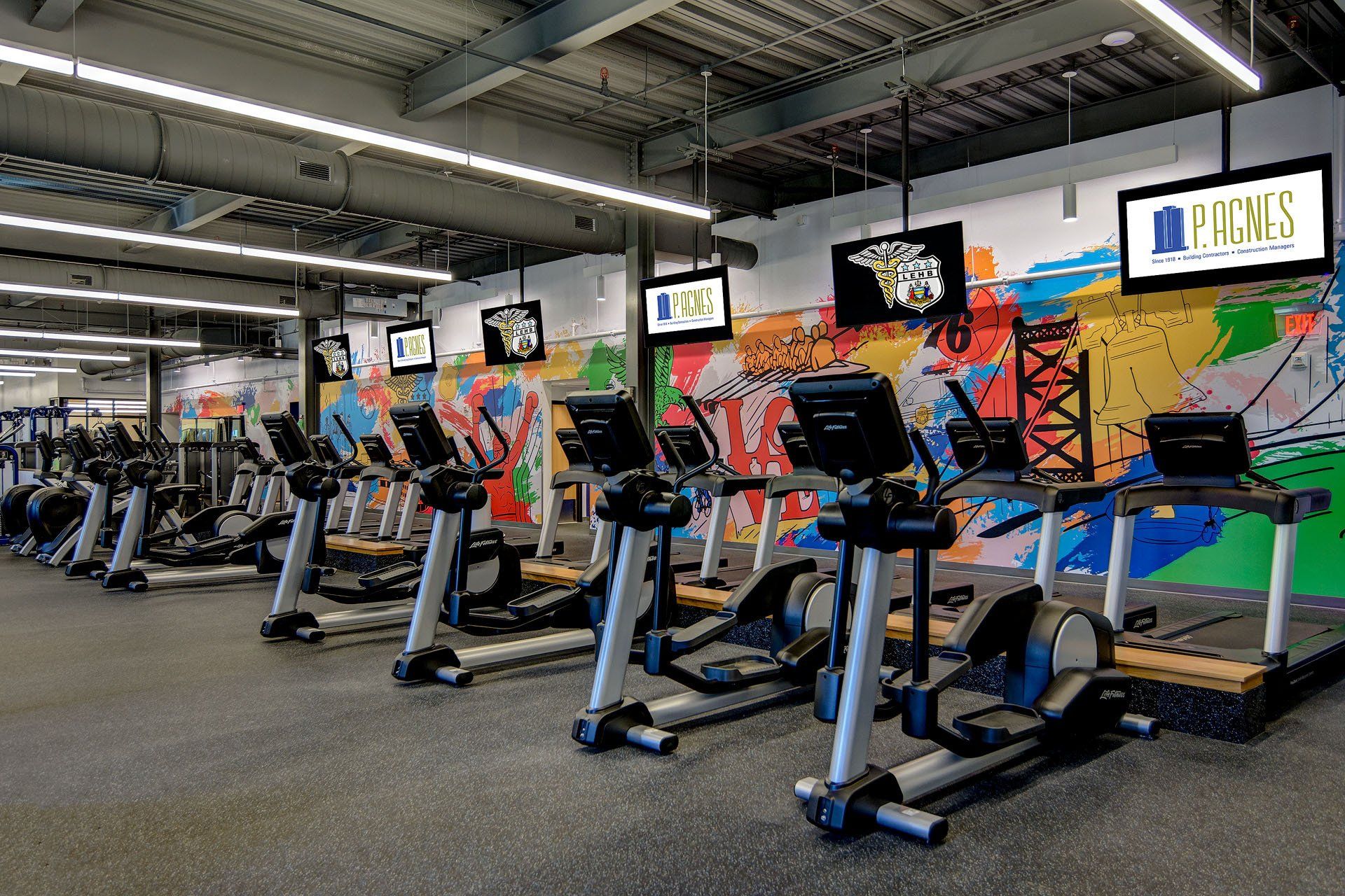 A row of treadmills and ellipticals in a gym with a mural on the wall.