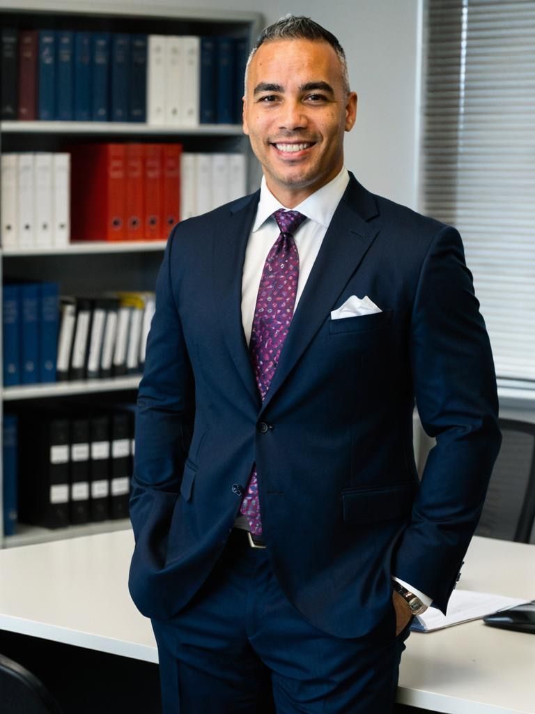 A man in a suit and tie is standing in front of a desk with his hands in his pockets.