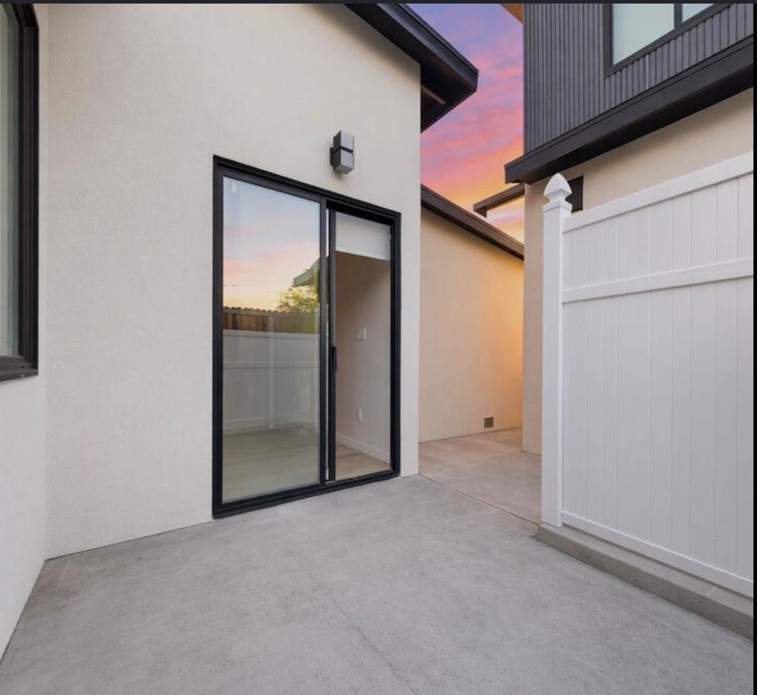Modern backyard patio between two houses with sliding glass door and white fence at sunset