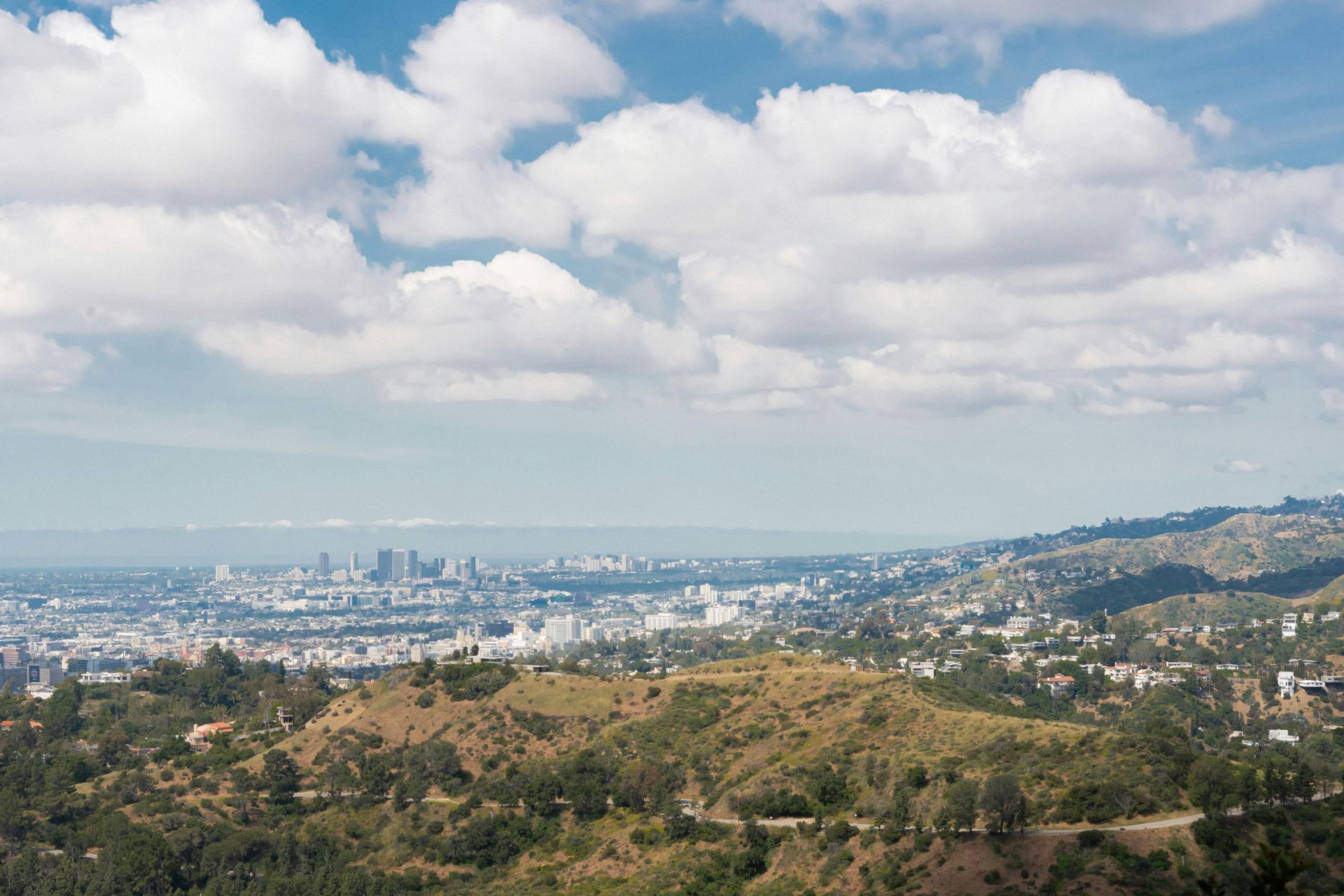 Wide city skyline beyond dry hills under a cloudy blue sky