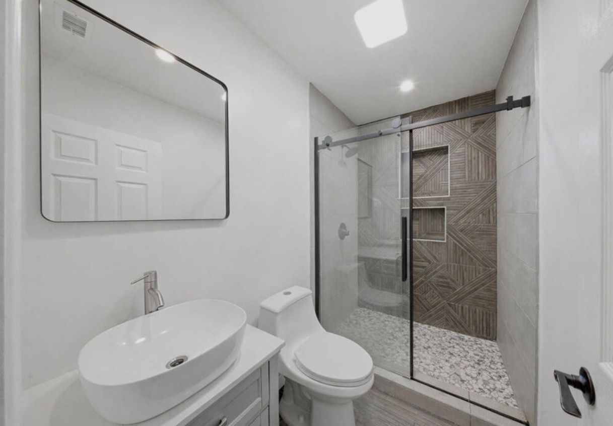 Modern bathroom with white sink, toilet, mirror, and glass shower with tiled walls