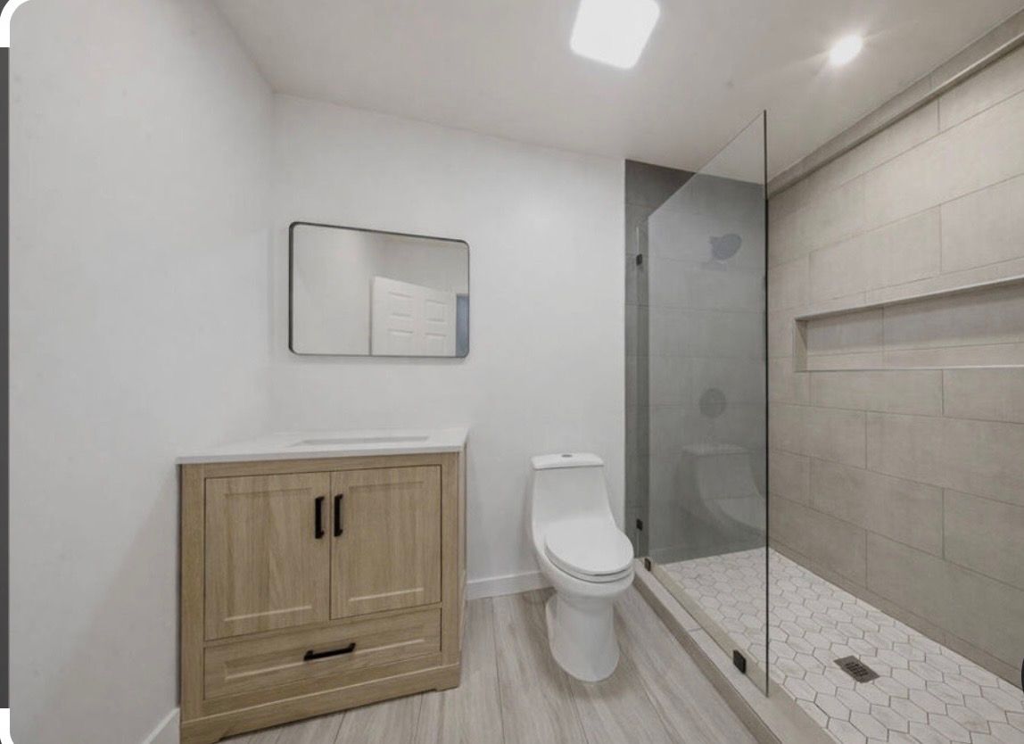 Modern bathroom with white walls, wood vanity, toilet, glass shower, and tiled shower niche
