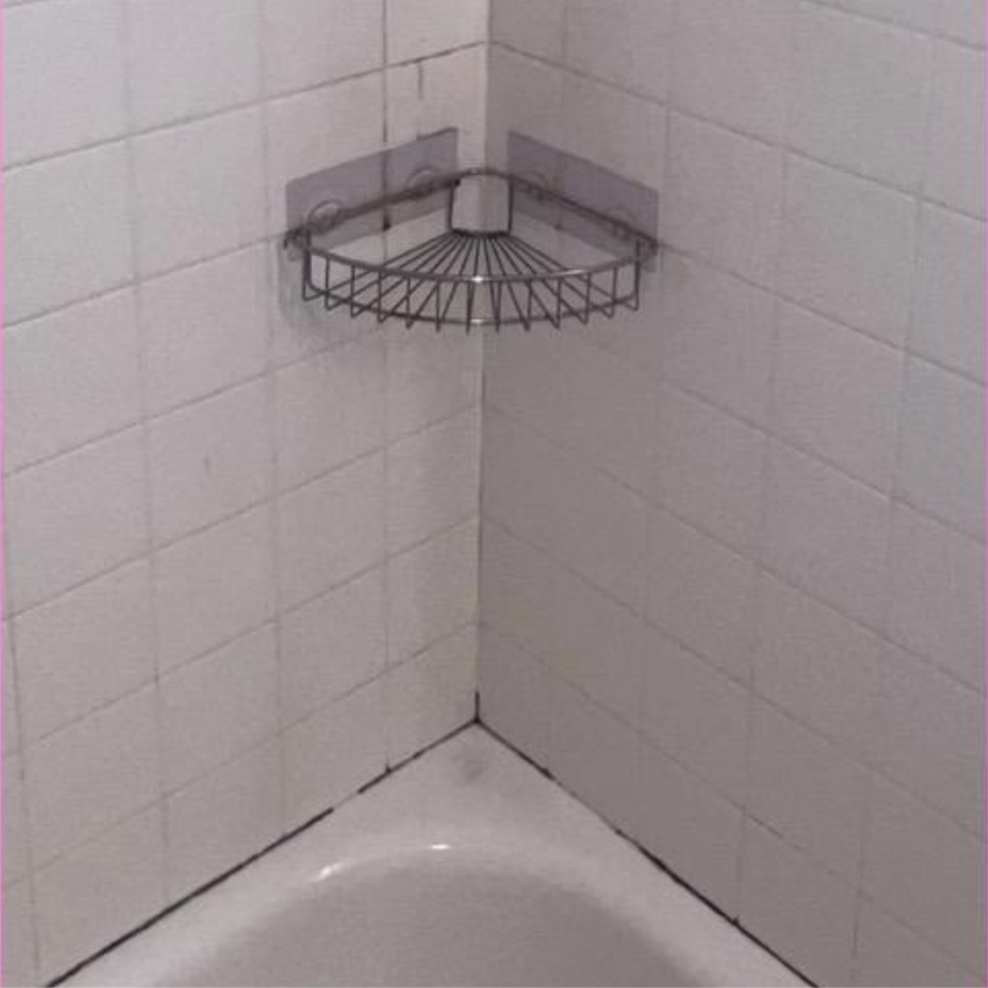 Corner shower with white tiled walls, chrome corner shelves, and part of a white tub below
