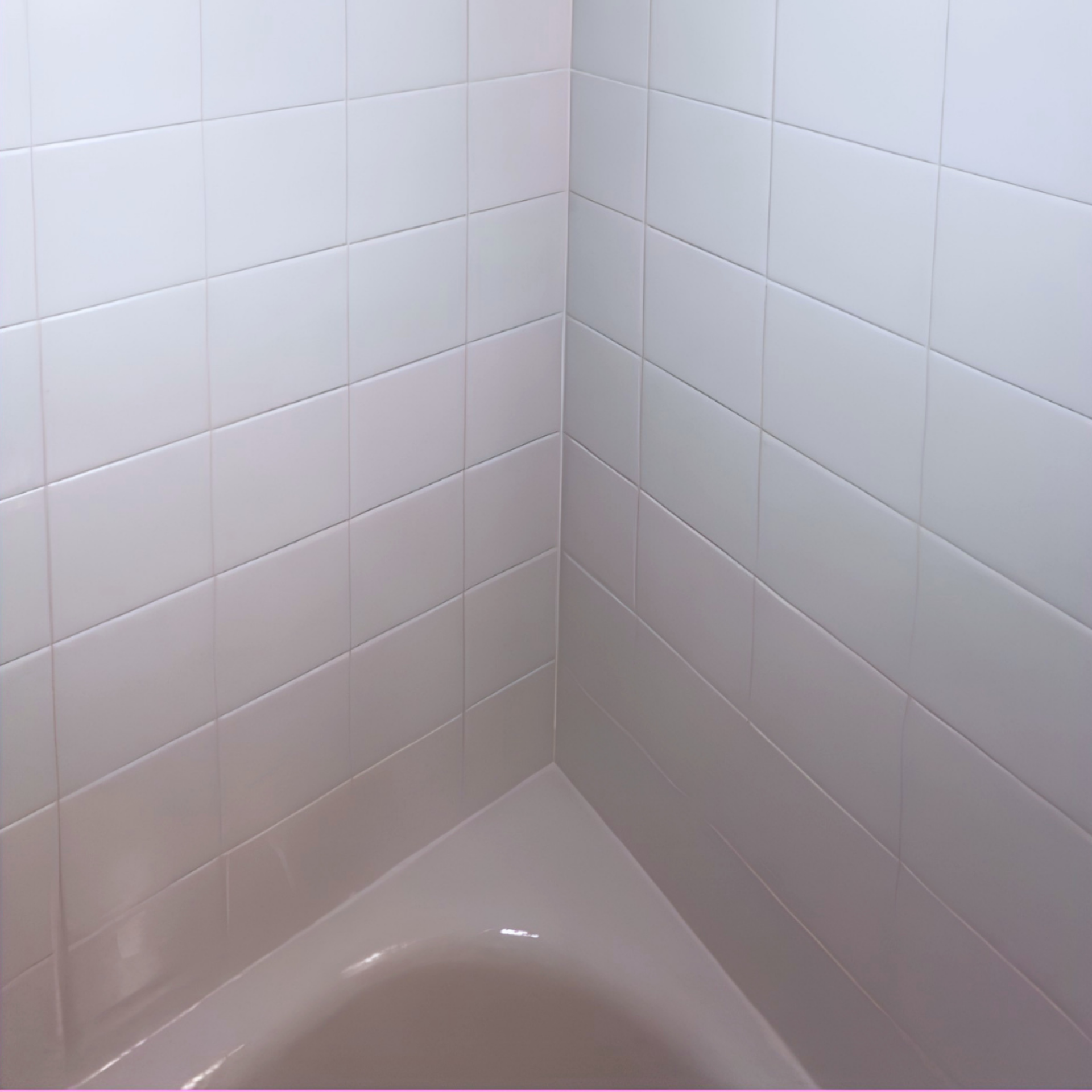 Corner of a white-tiled shower with a white bathtub edge visible at the bottom