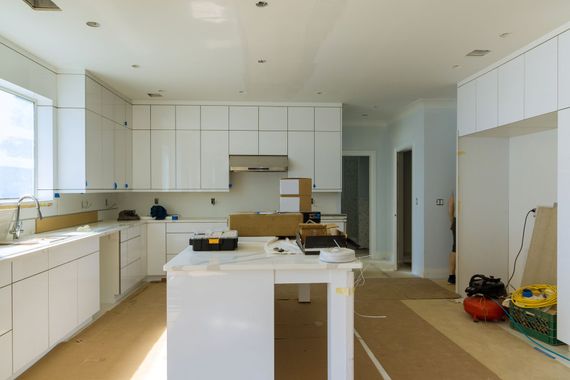 Bright modern kitchen with white cabinets, island, and countertop items; boxes on the floor near the right wall.