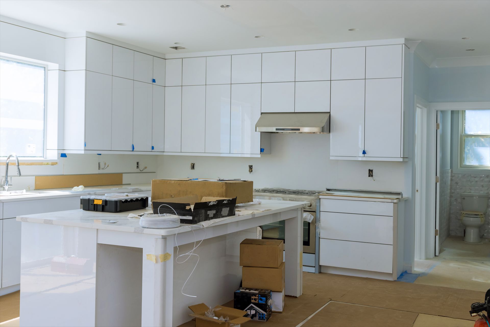 Bright kitchen under renovation with white cabinets, granite island, and boxes on the floor