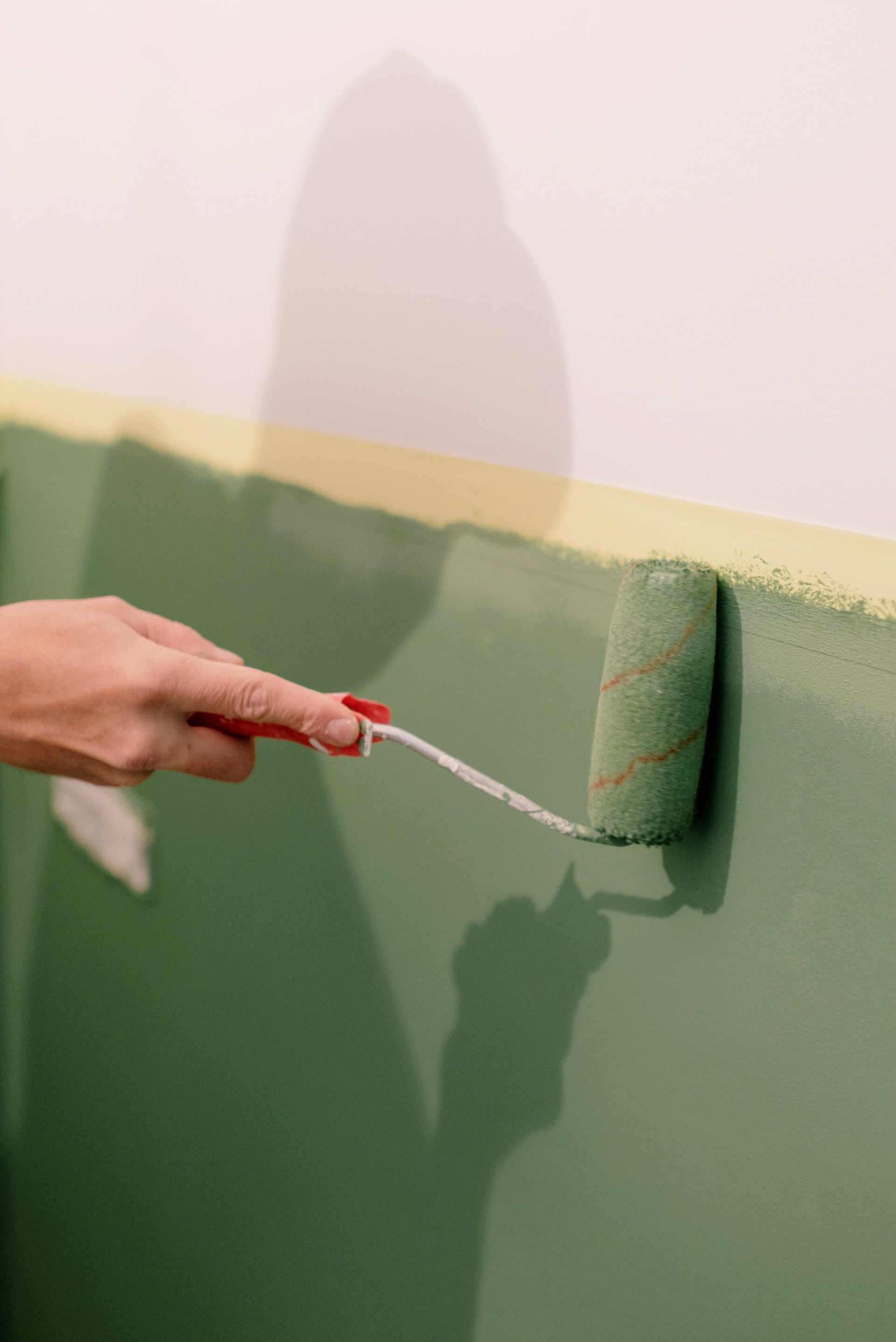 Person painting a gray wall with a roller indoors, covering a patchy surface.