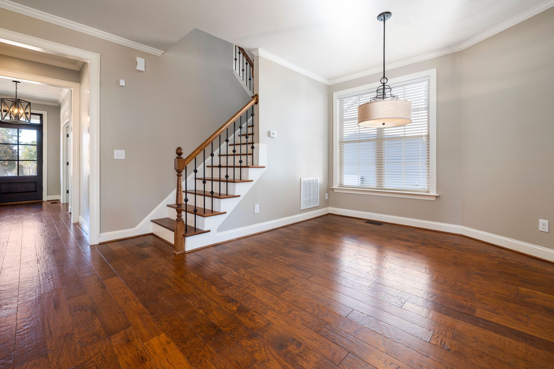 Empty living room with hardwood floors, staircase, and window with hanging light fixture