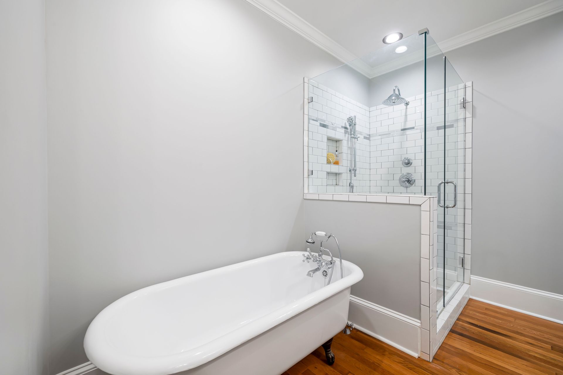 Bright modern bathroom with a freestanding tub and glass-enclosed shower on wood flooring.