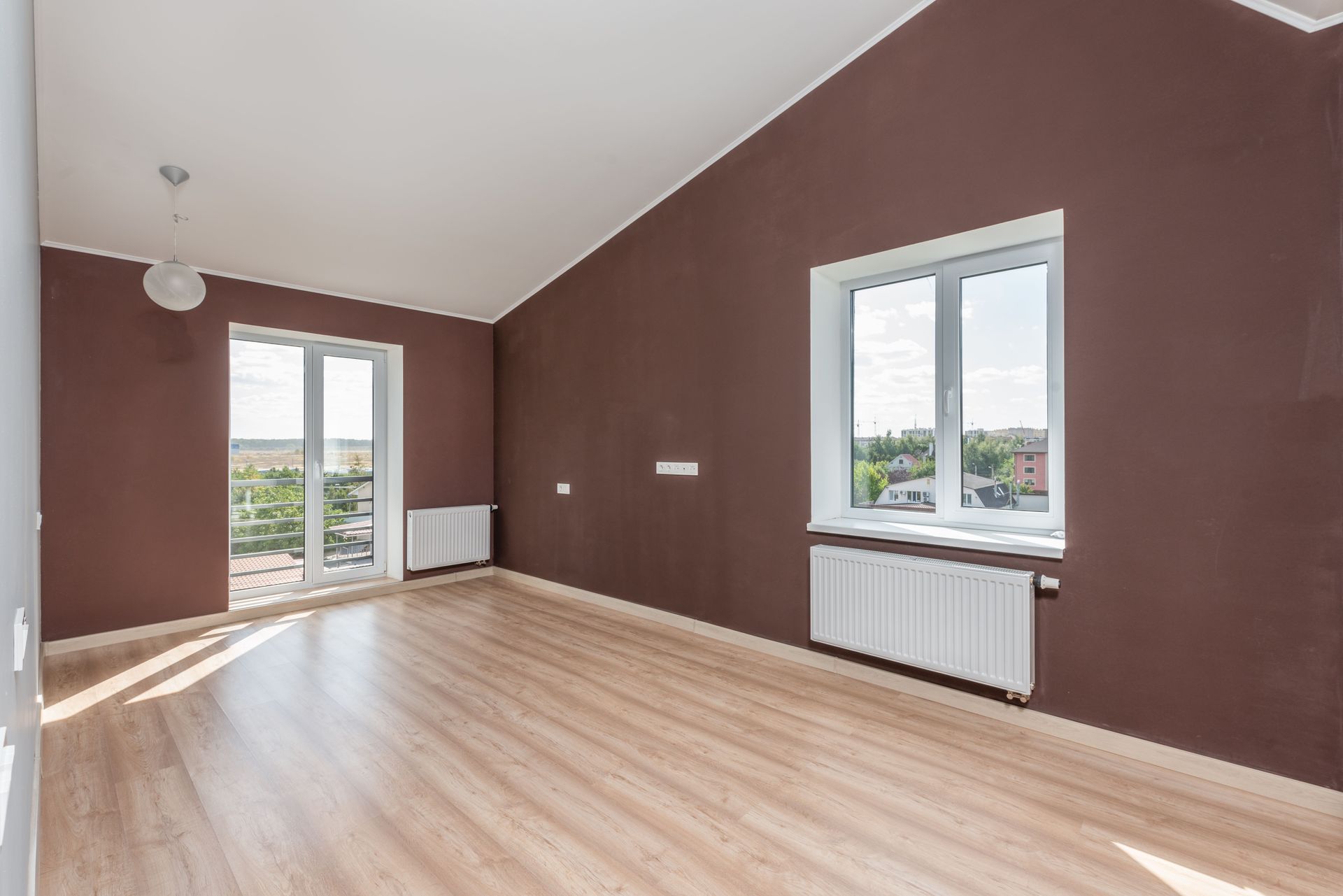Empty room with brown walls, light wood flooring, and windows letting in daylight.