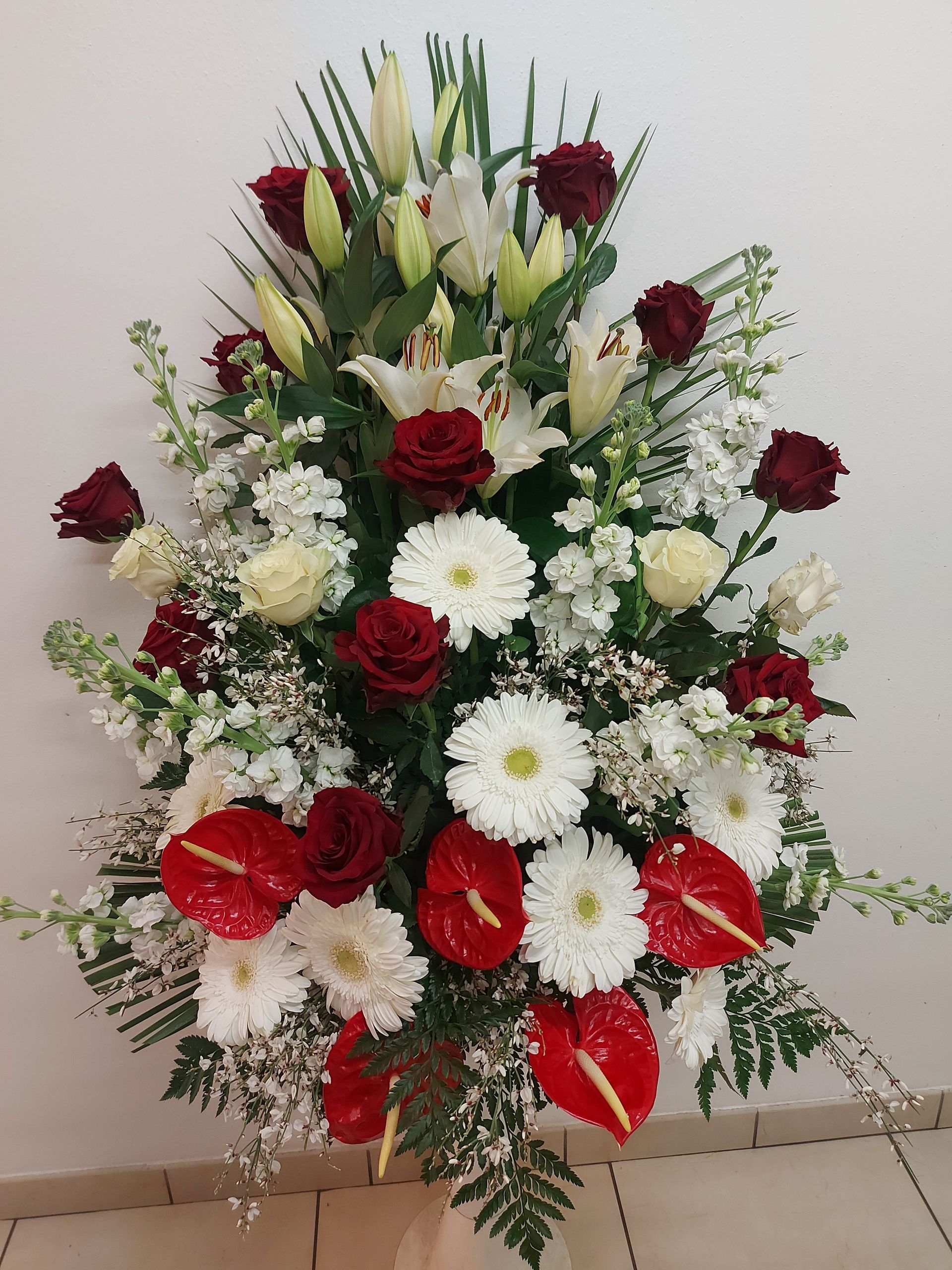 Composizione di rose rosse, gigli bianchi, gerbere e fiori di anthurium rossi in esposizione.