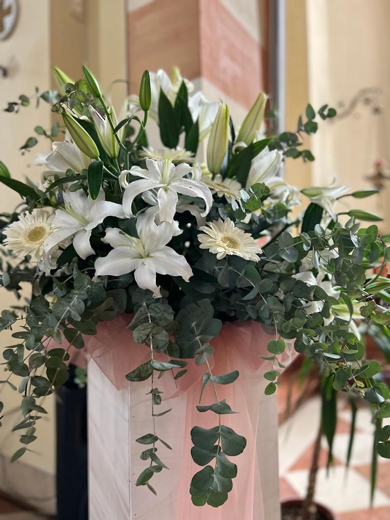 Gigli bianchi e margherite in una composizione con verde di eucalipto e tessuto rosa su un pilastro.