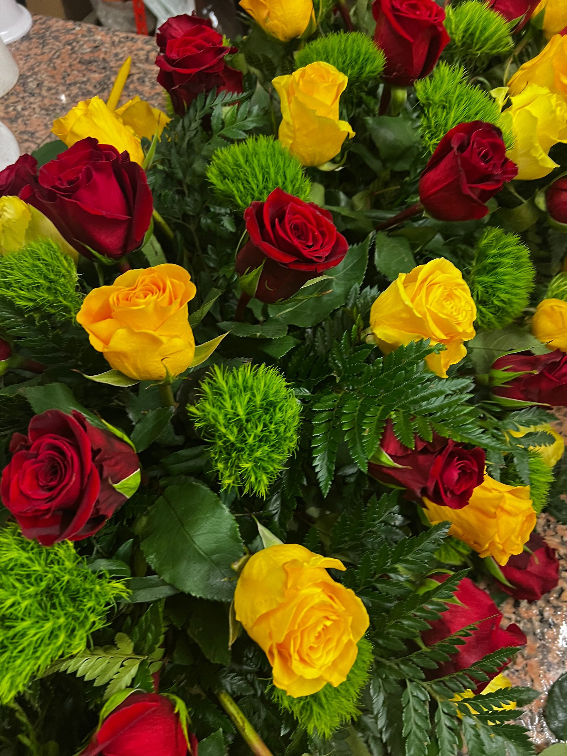 Rose rosse e gialle con accenti verdi in una composizione floreale.