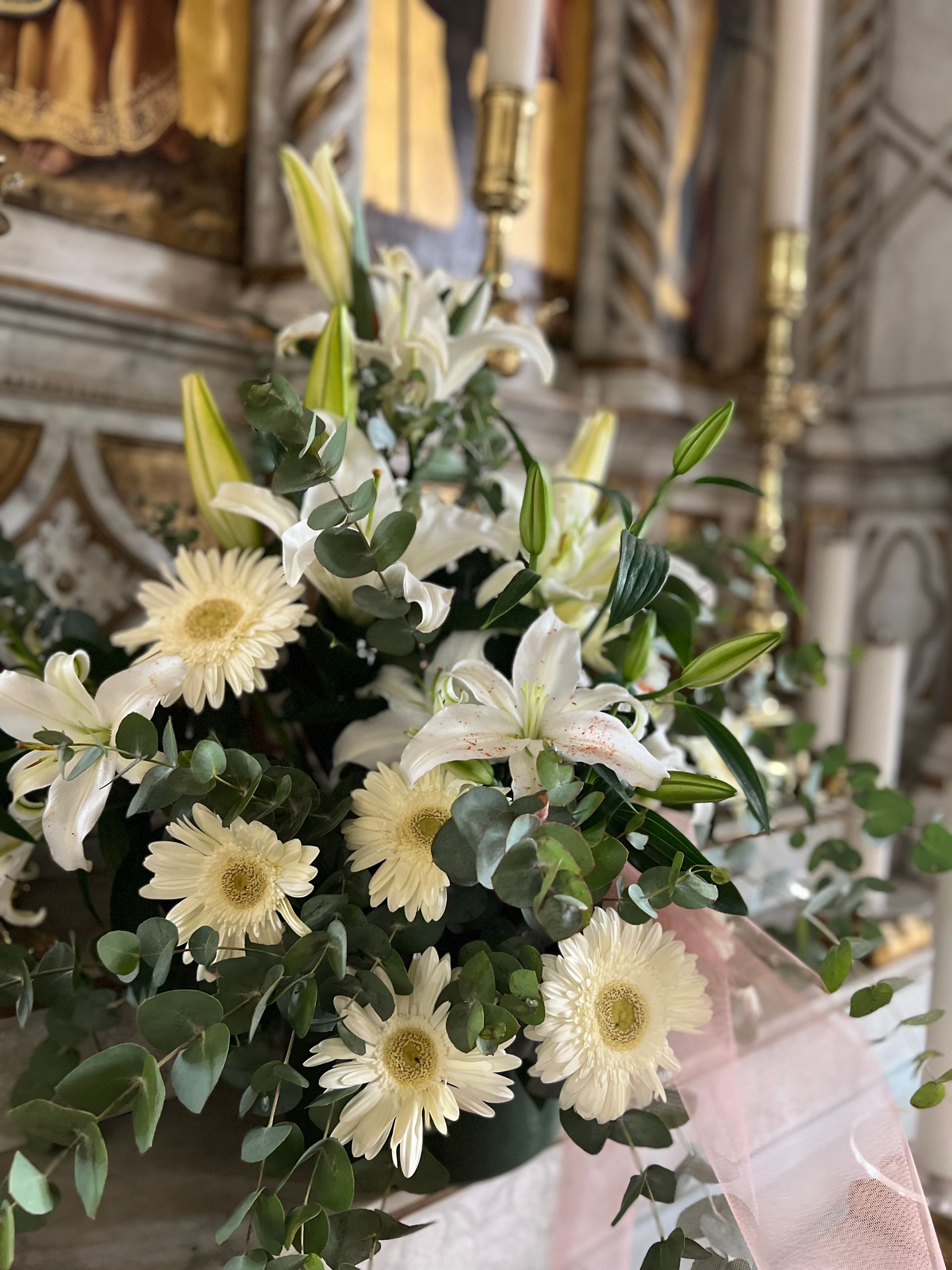 Gigli bianchi e margherite con verde in una chiesa, decorata con un nastro rosa.