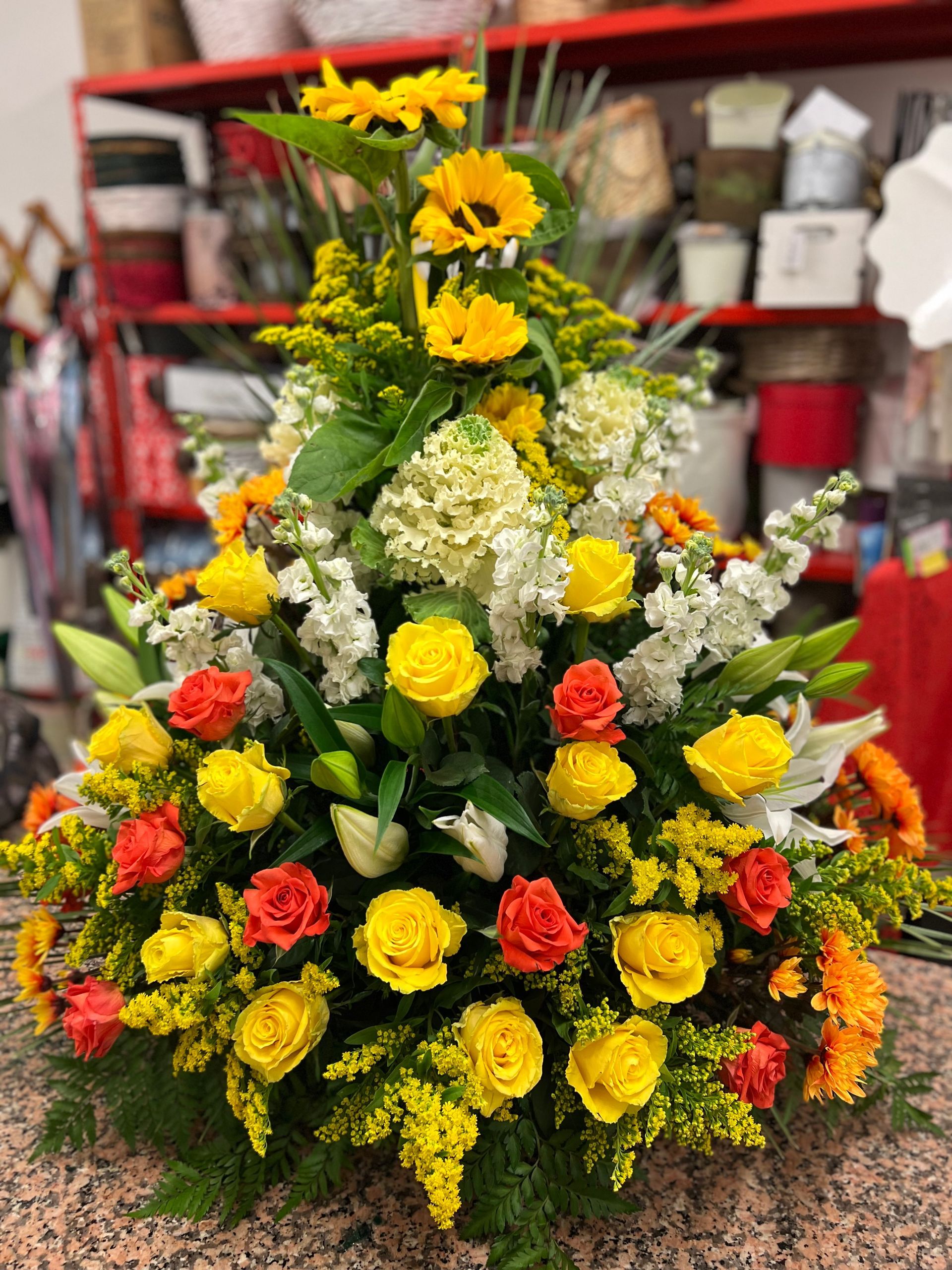 Composizione floreale luminosa con rose gialle e arancioni, girasoli e fiori bianchi.